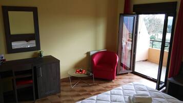 Habitación de hotel con cama, una silla roja, una mesita, un espejo y una puerta corrediza de vidrio que da a un balcón.