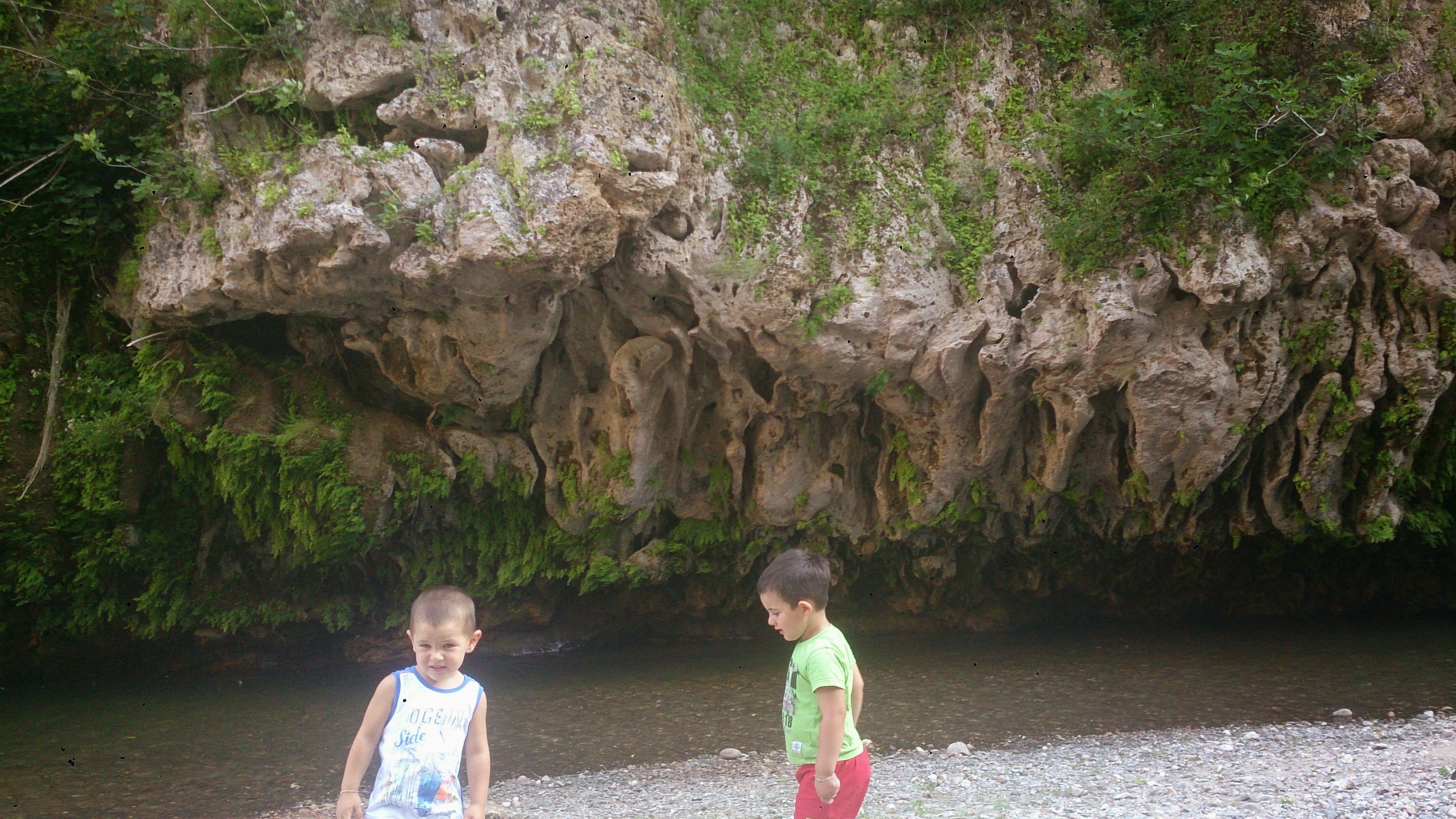 Dos nens al costat d'un riu, amb un penya-segat rocos en el fons.