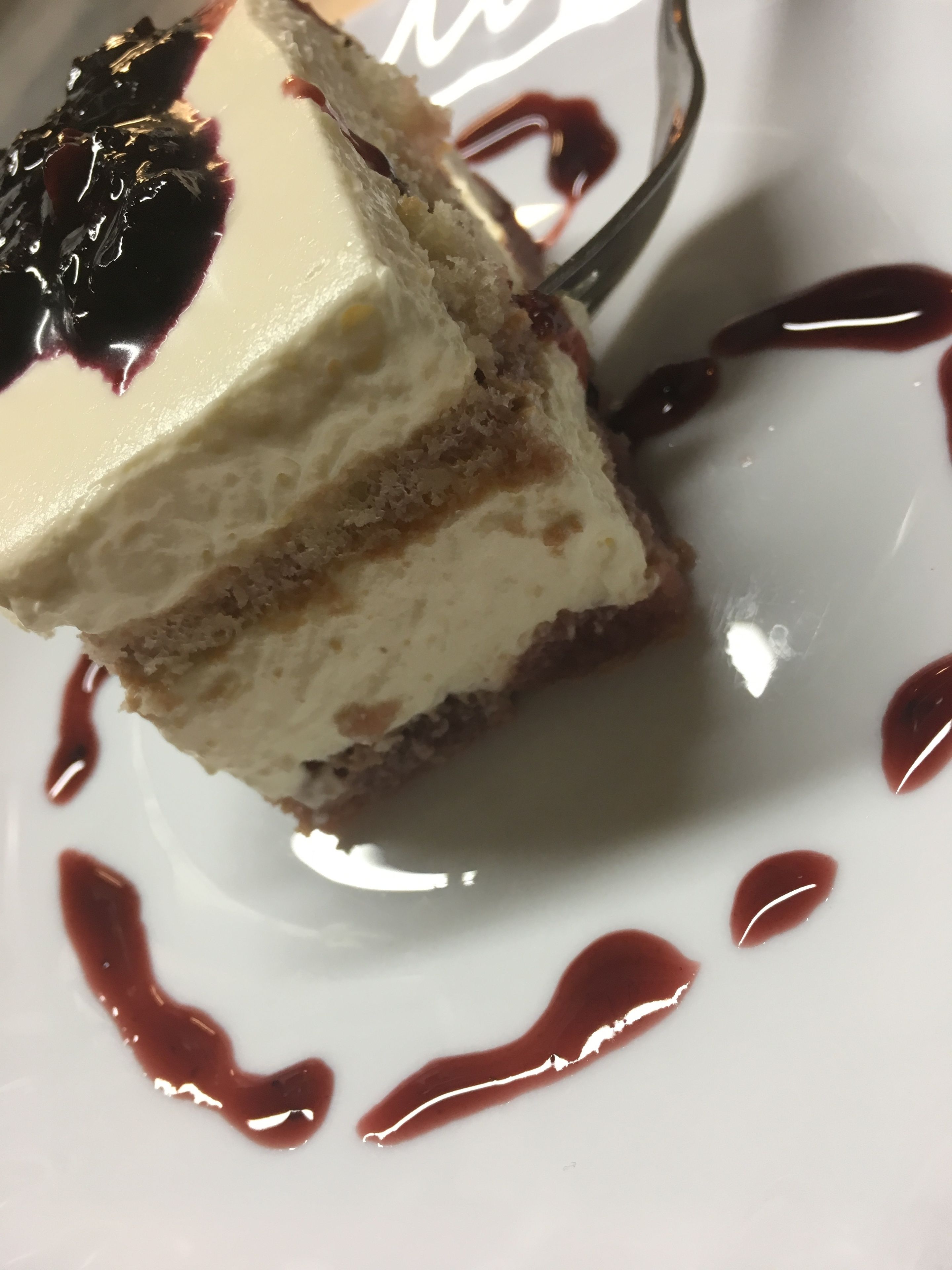Una porción de pastel con una capa cremosa y cobertura oscura, servida en un plato blanco con salsa brillante.