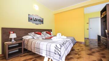 Quarto de hotel com cama, mesa de cabeceira, abajur, um quadro na parede e guarda-roupa de madeira.