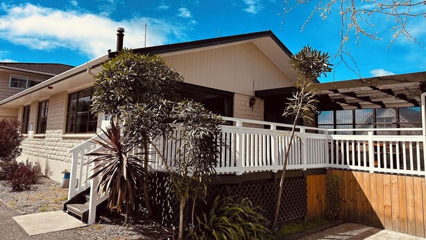 A two-story house with a balcony, a stone wall, and a wooden fence. - Cherylea Motel (Blenheim)