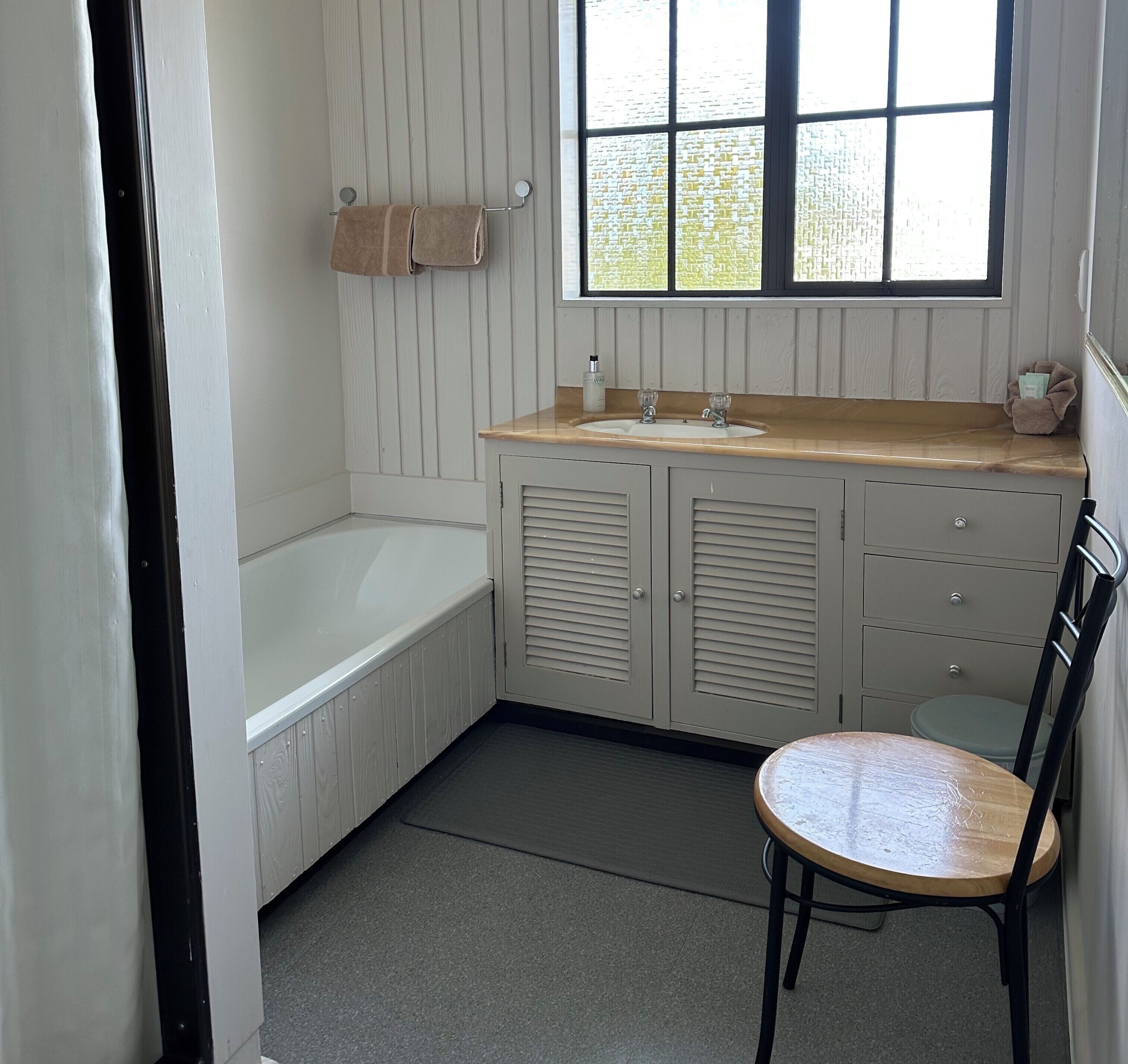 Une salle de bain avec une baignoire, un lavabo et une chaise.