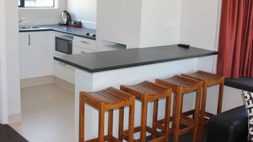 Une cuisine moderne avec des armoires blanches, un comptoir noir et un four à micro-ondes encastré. On y trouve trois tabourets en bois devant le comptoir.