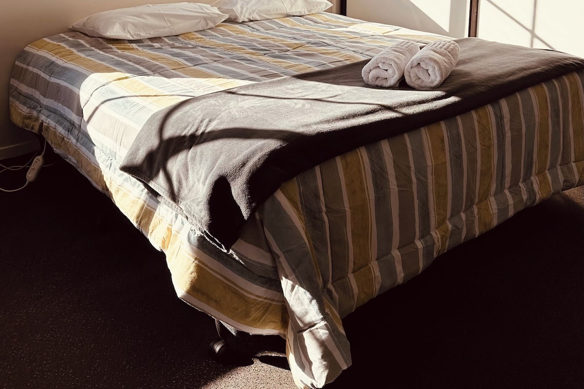 A bed with a striped bedspread, two pillows, and rolled towels on it.