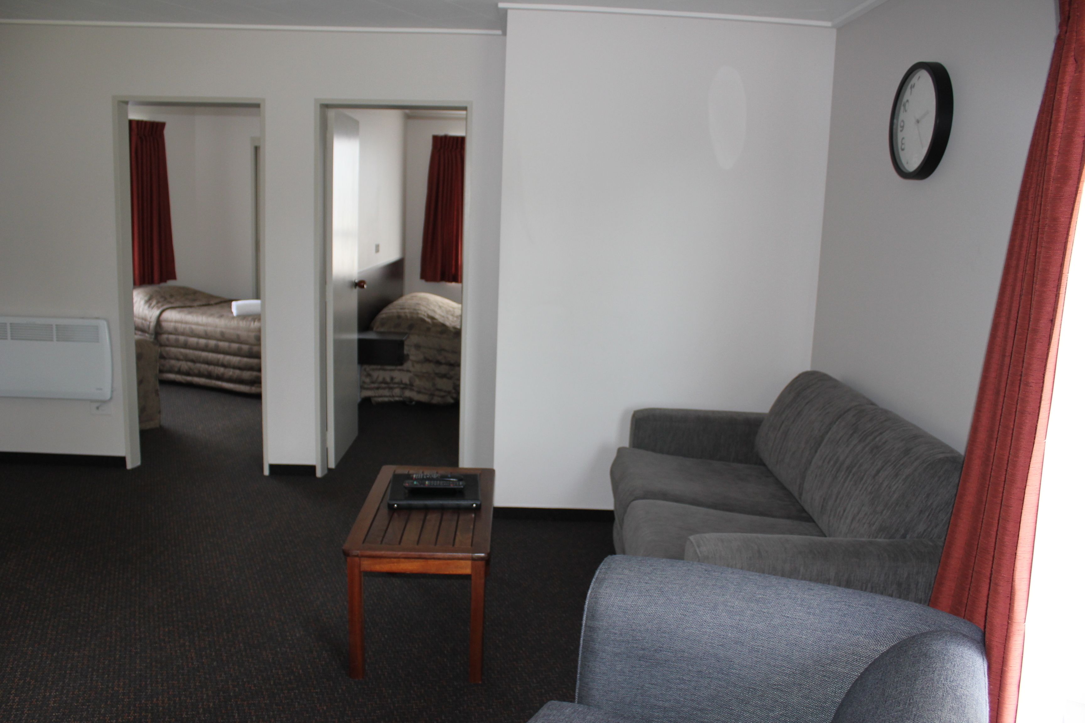 A hotel room with a grey sofa, a wooden coffee table, and a bed with red curtains.