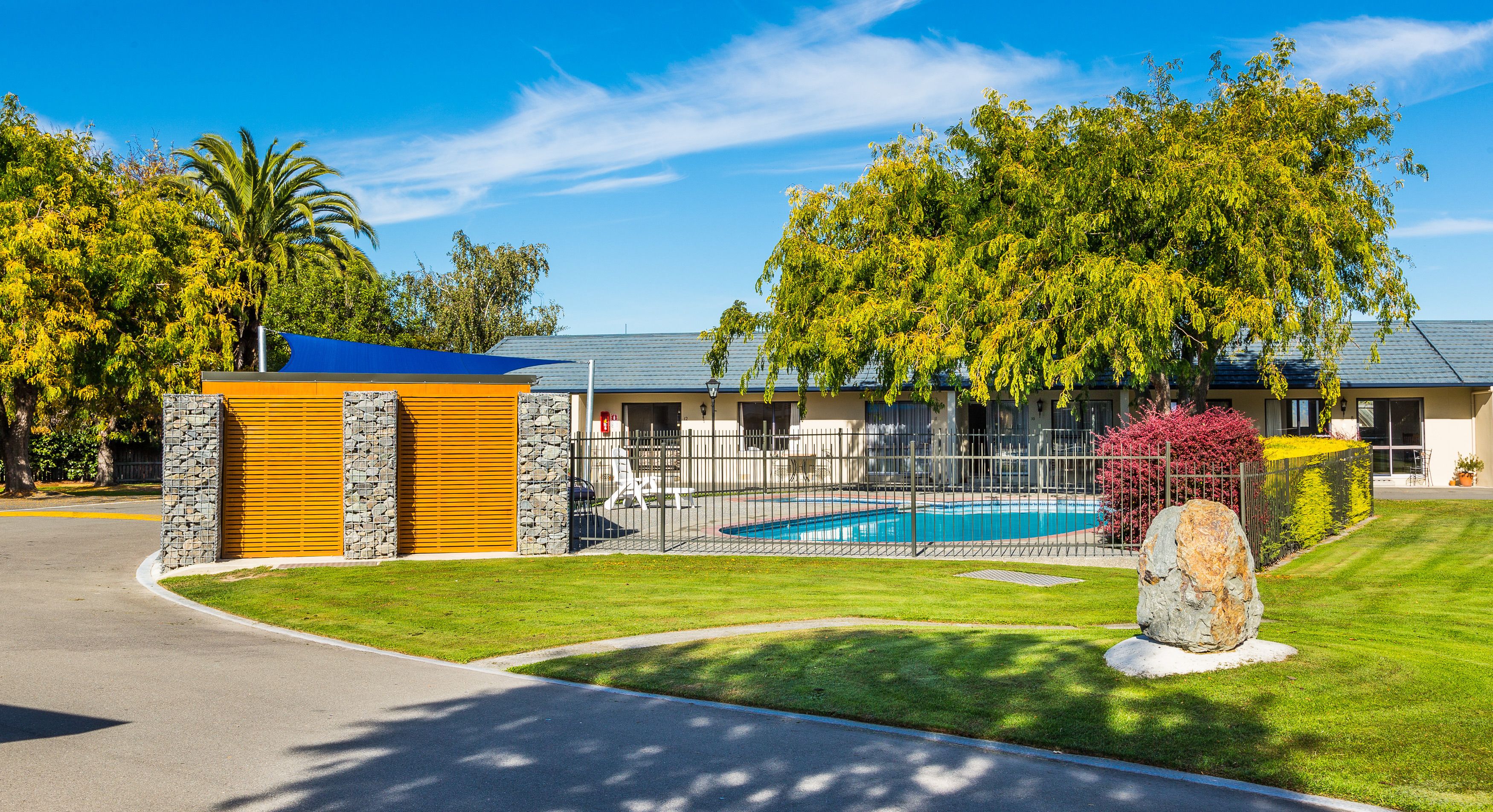 Una propiedad residencial con piscina, fachada de piedra y madera, y césped bien cuidado.