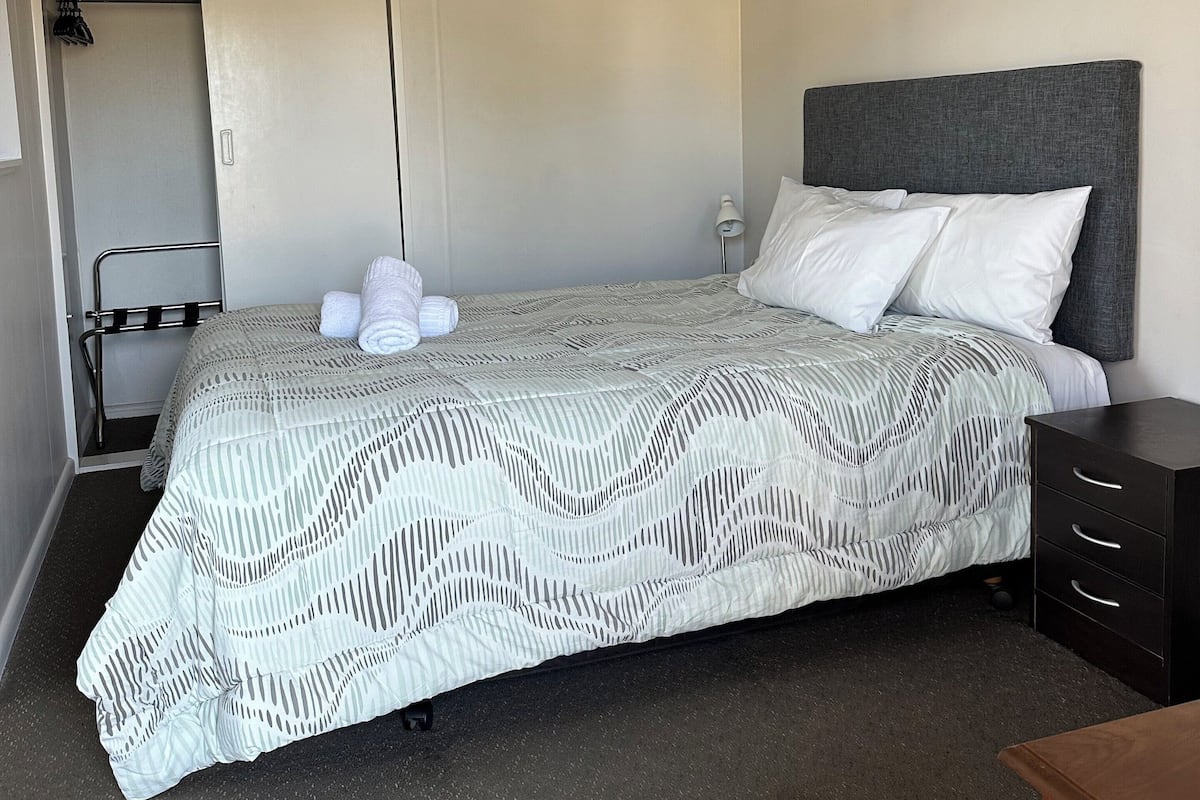 A neatly made bed with a patterned bedspread, a bedside table, and a wardrobe with a hanging rack.