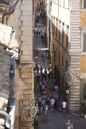 Una stretta via con pedoni, edifici storici e un muro di pietra.