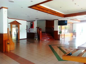 A spacious lobby with a wooden staircase, a reception desk, and a fire extinguisher on the wall. - Sanbay Hotel (Sandakan)