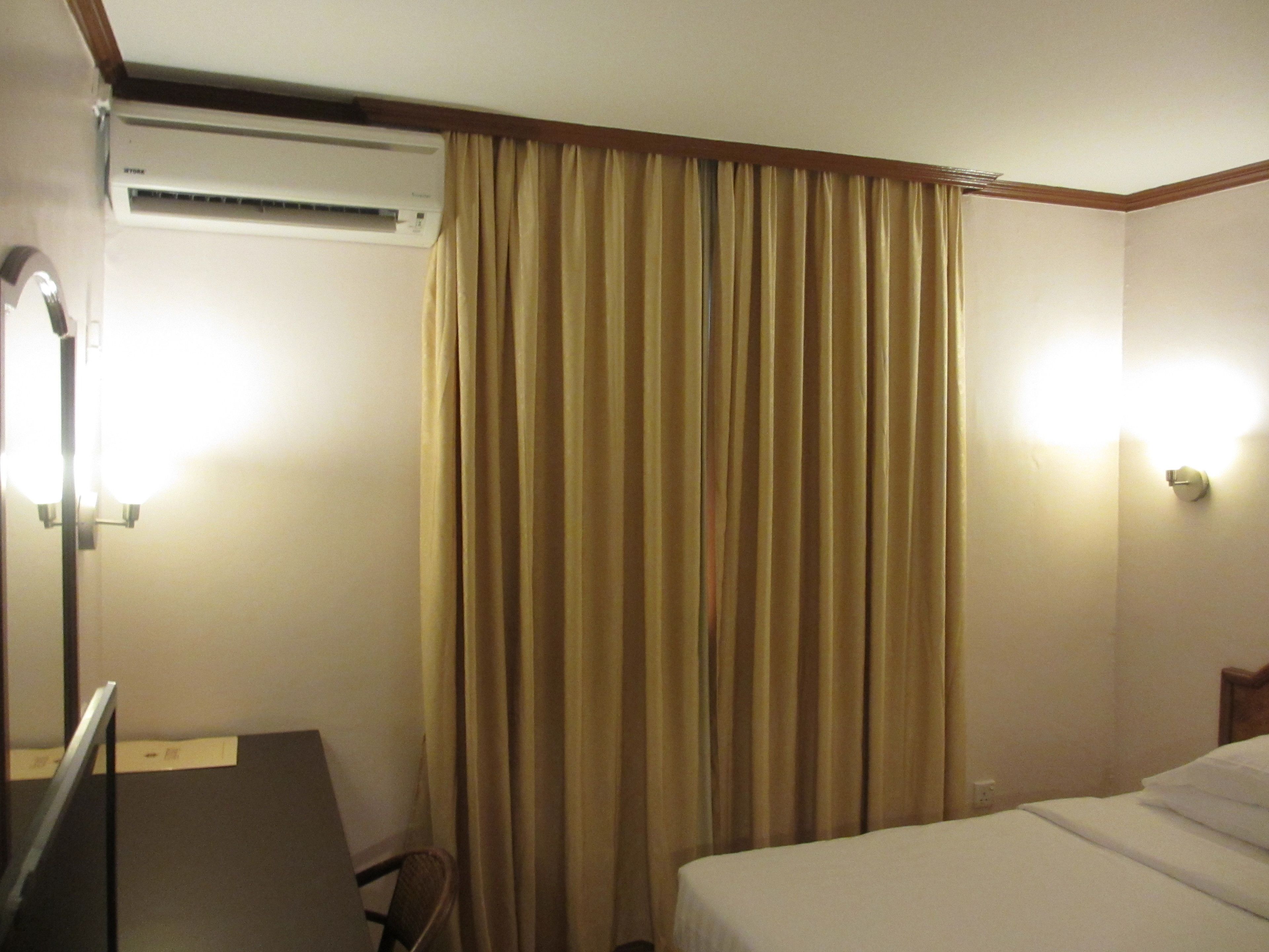 Una habitación de hotel con una cama, un escritorio, una silla, una cortina y un equipo de aire acondicionado.