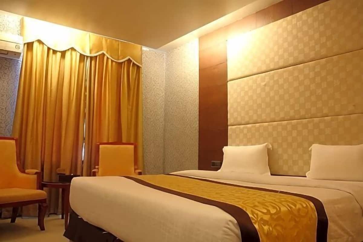 Una habitación de hotel con una cama grande, dos sillas, una mesita y una cortina.