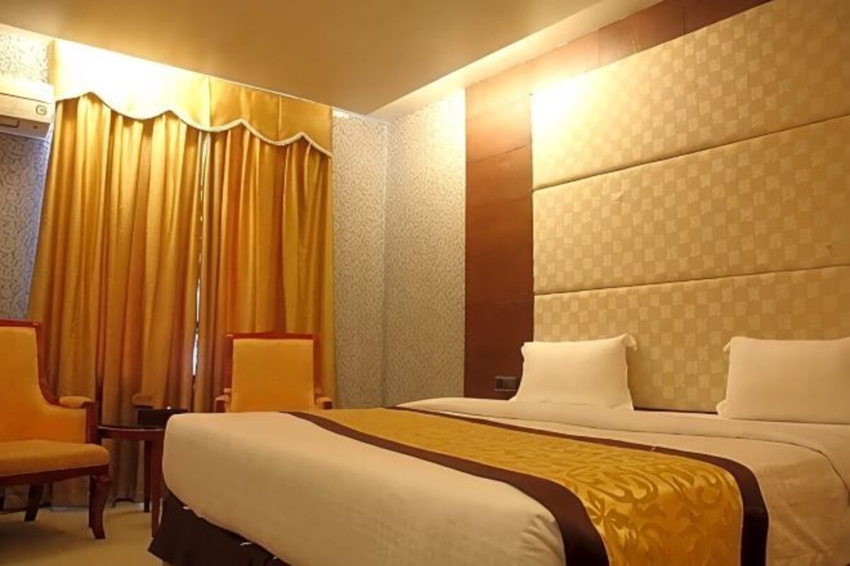 A hotel room with a large bed, two chairs, a small table, and a curtain.
