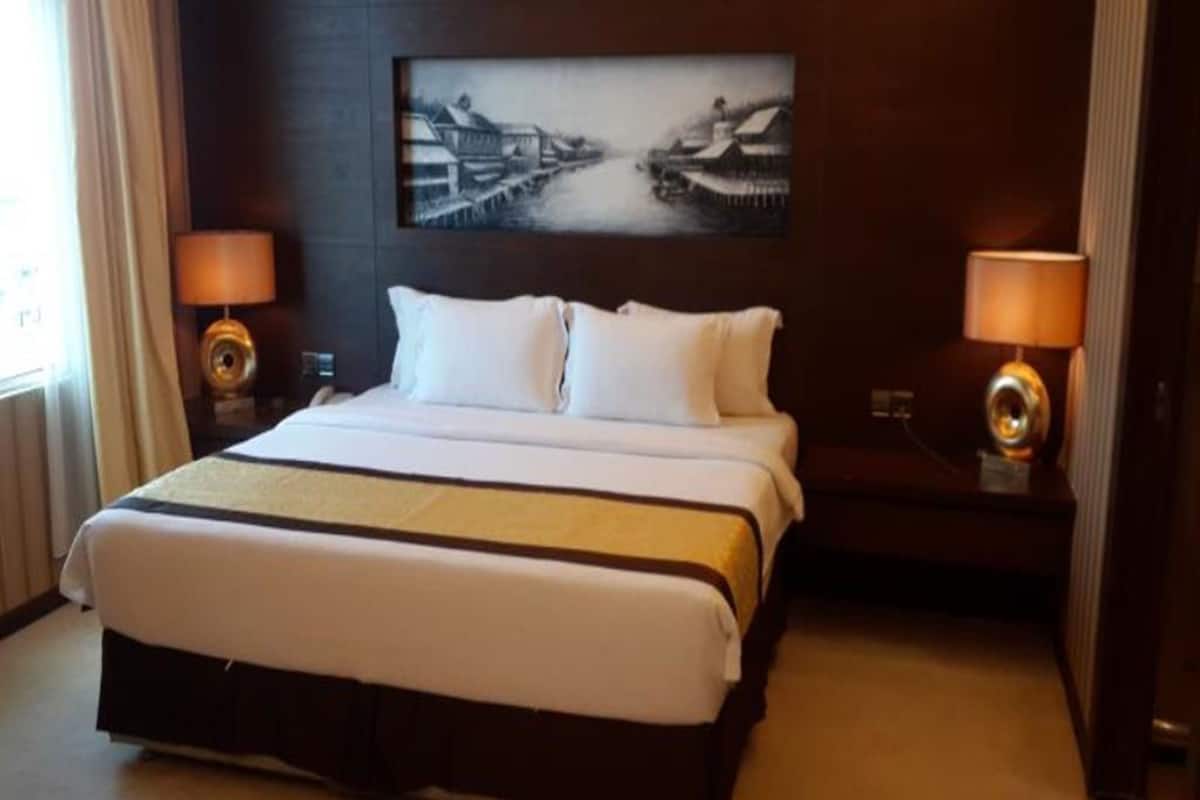 Una habitación de hotel con una cama grande, dos lámparas de noche, un cuadro en la pared y una ventana con cortinas.