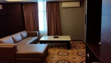 A living room with a brown sofa, a small coffee table, patterned carpet, and a wall-mounted air conditioner.