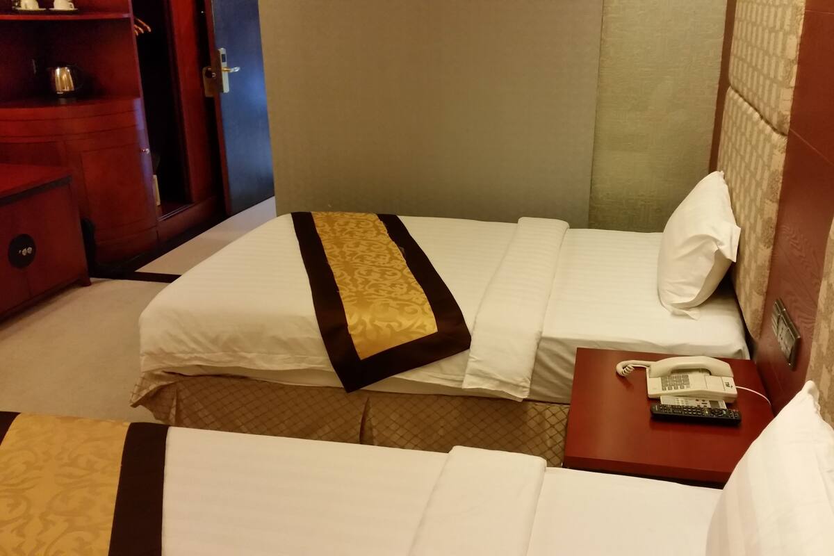Habitación de hotel con dos camas, una mesita de noche con teléfono y controles remotos, una mesita auxiliar de madera y un armario.