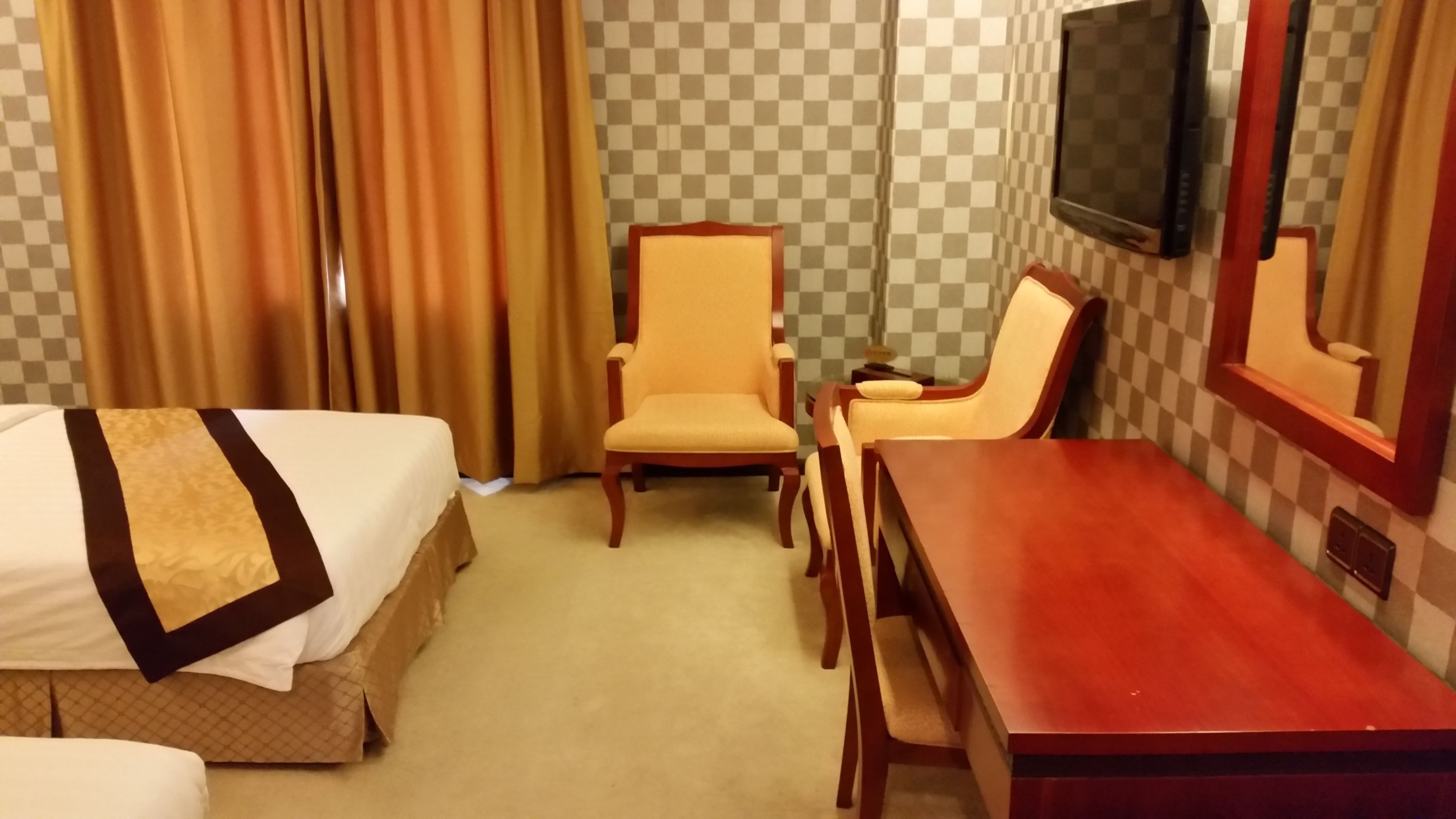 A hotel room with a bed, a wooden desk, two chairs, a television, and curtains.