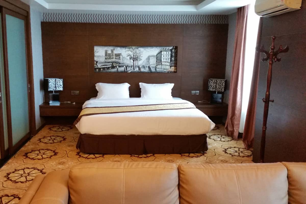 Habitación de hotel con una cama grande, dos mesitas de noche con lámparas, un cuadro colgado en la pared y una alfombra estampada.