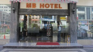MB Hotels exteriör har en modern fasad, stora glasfönster och en röd matta som leder fram till entrén.