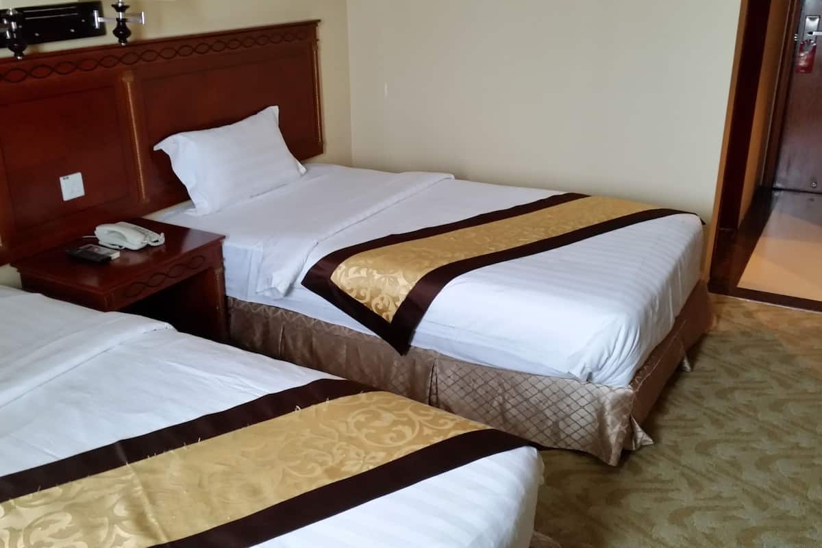 Una habitación de hotel con dos camas, cabecero de madera, mesita de noche con teléfono y suelo alfombrado.