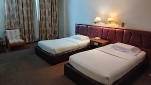 Une chambre d’hôtel avec deux lits, une tête de lit en bois, une table de chevet avec une lampe et une chaise recouverte d’un tissu à motifs floraux.
