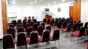 Une salle de conférence avec des rangées de chaises rouges, un tableau blanc, un pupitre et un écran de télévision.