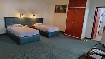A hotel room with two beds, a wardrobe, a painting on the wall, and a desk with a chair.