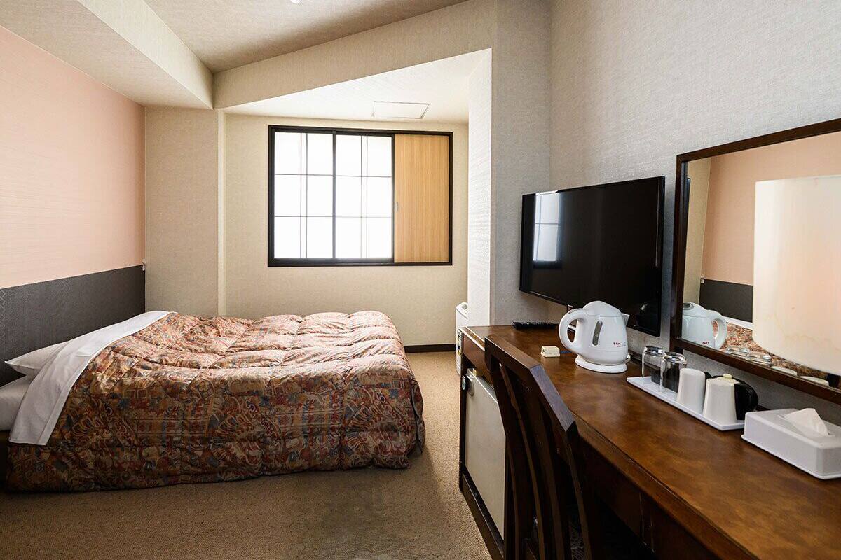 A hotel room with a bed, a desk with a TV, a coffee maker, and a mirror.