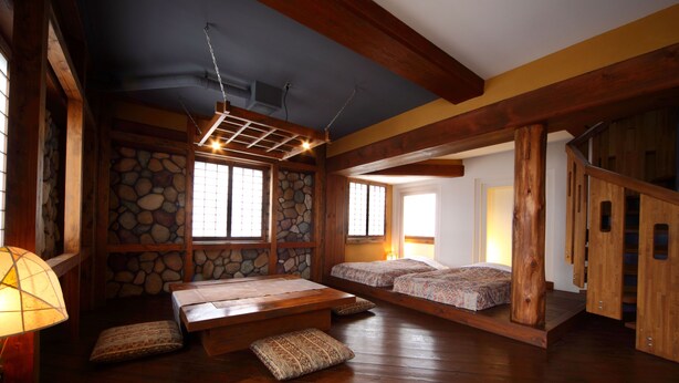 A traditional Japanese-style room with tatami flooring, a low wooden ceiling, and a stone wall. There are two tatami mats with cushions, a low wooden table, and a hanging light fixture. - Hotel Asyl Nara (Nara)