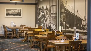 Uma área de refeições com mesas e cadeiras de madeira, um mural preto e branco na parede e uma placa indicando o preço de $10.