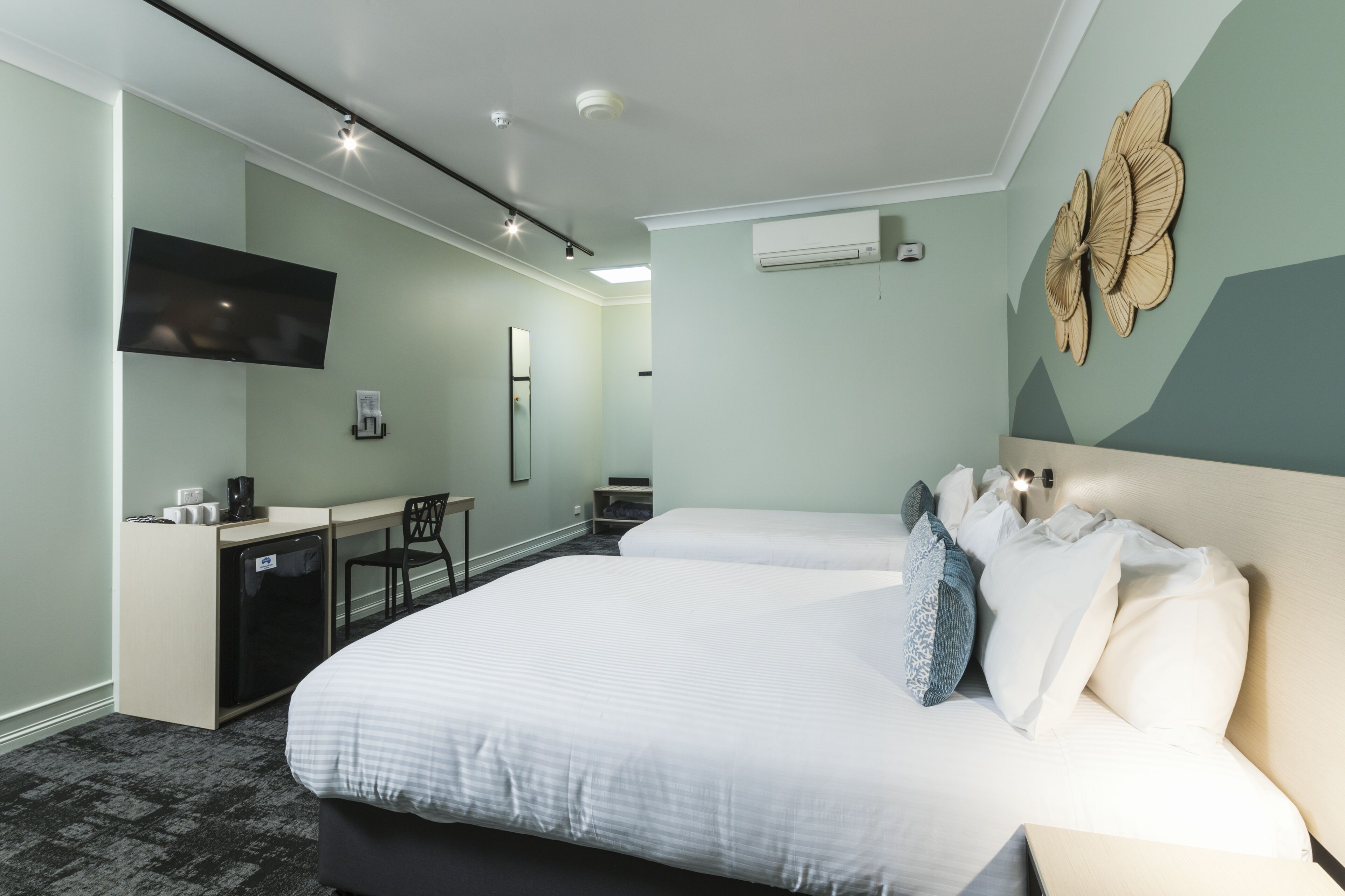 A hotel room with a large bed, a desk, a chair, a flat-screen TV, and an air conditioning unit.