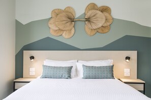 A neatly made bed with patterned pillows, a wall-mounted light fixture, and a decorative wall piece. - Nightcap at Atherton Hotel (Atherton)