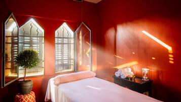 A room with a bed, a small table with a lamp, and a window with a plant.