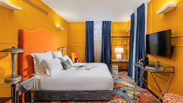 Una habitación de hotel con una cama grande, un escritorio con lámpara, televisión y alfombra estampada.