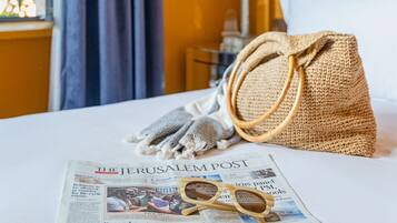A bed with a newspaper, a pair of sunglasses, and a woven bag on it.