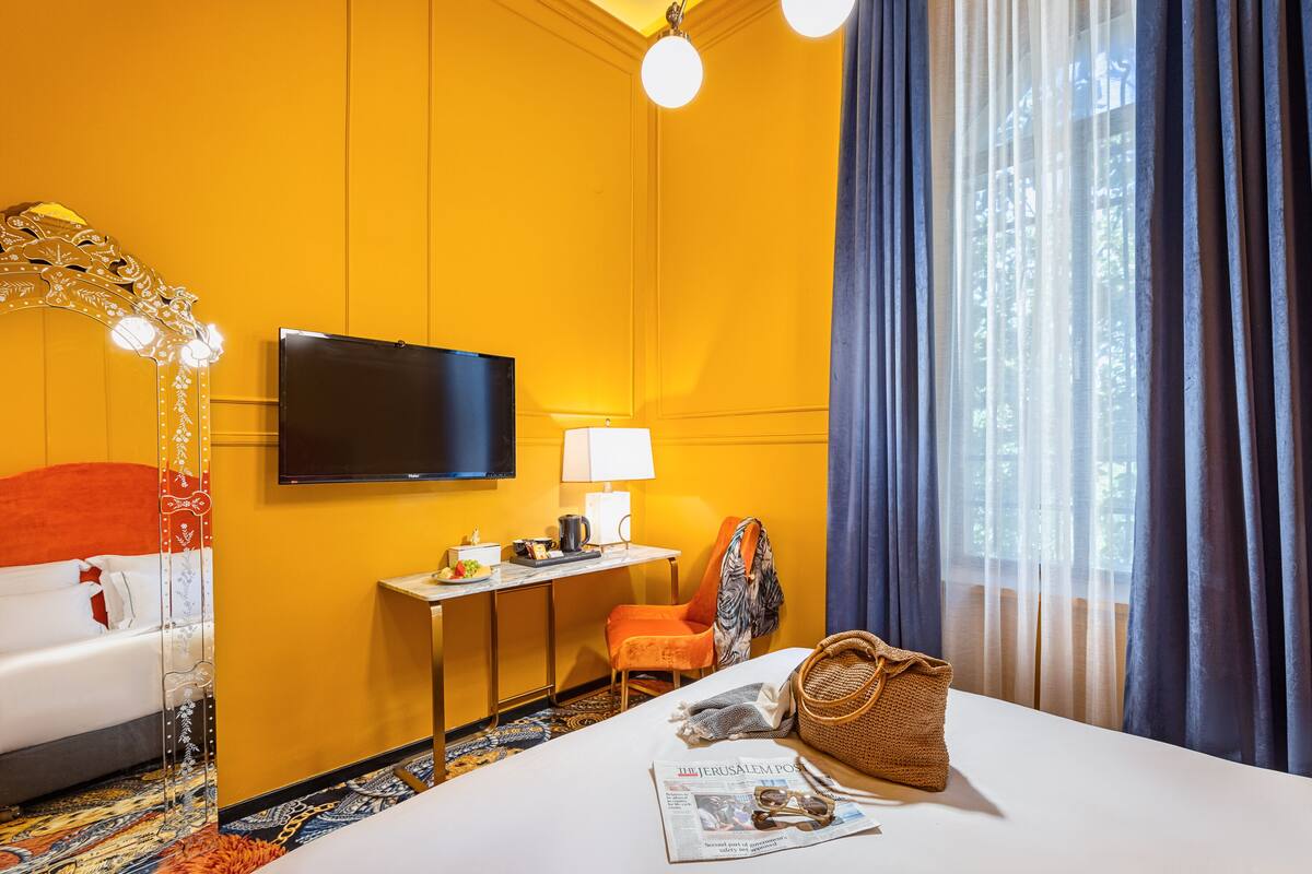 Une chambre d’hôtel avec un lit, un bureau, une télévision, une lampe et une fenêtre avec des rideaux.