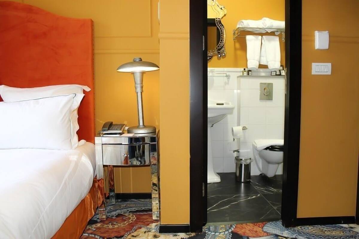 Une chambre d’hôtel avec un lit, une table de chevet, une lampe et une salle de bain visible à travers une porte ouverte.