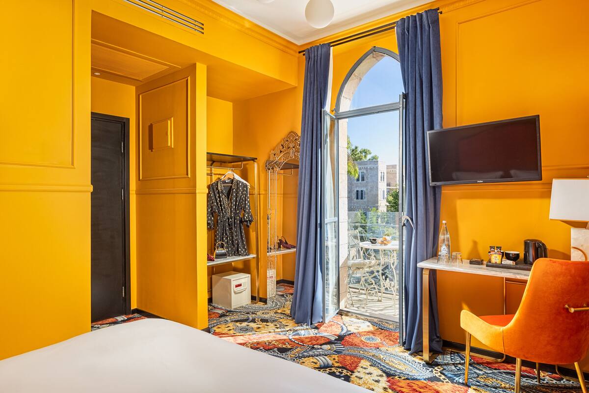 Une chambre d’hôtel avec un grand lit, un bureau avec une chaise, une télévision et une vue sur la ville grâce à une grande fenêtre.