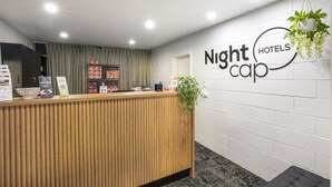 Un mostrador de recepción con detalles de madera, un letrero en la pared que dice "Nightcap Hotels" y una planta en maceta colgando del techo.