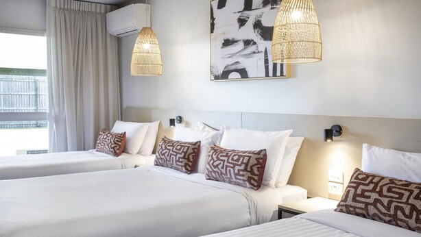 Habitación de hotel con dos camas, un ventanal con cortinas, aire acondicionado de pared y un cuadro abstracto grande.