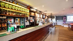 Zona de bar con mostrador, estantes llenos de botellas de licores y un cartel anunciando bandas en vivo.