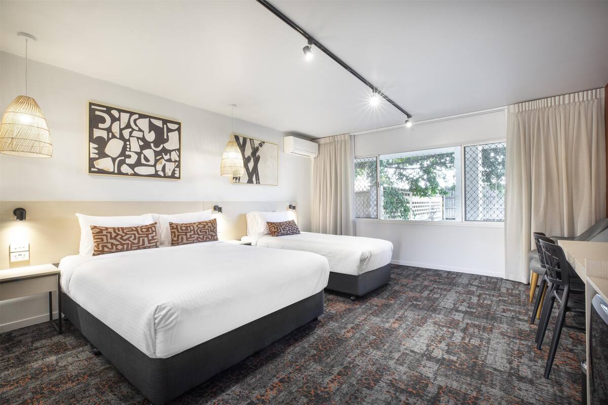 Ein Hotelzimmer mit zwei Betten, einem Schreibtisch und einem großen Fenster mit Vorhängen.