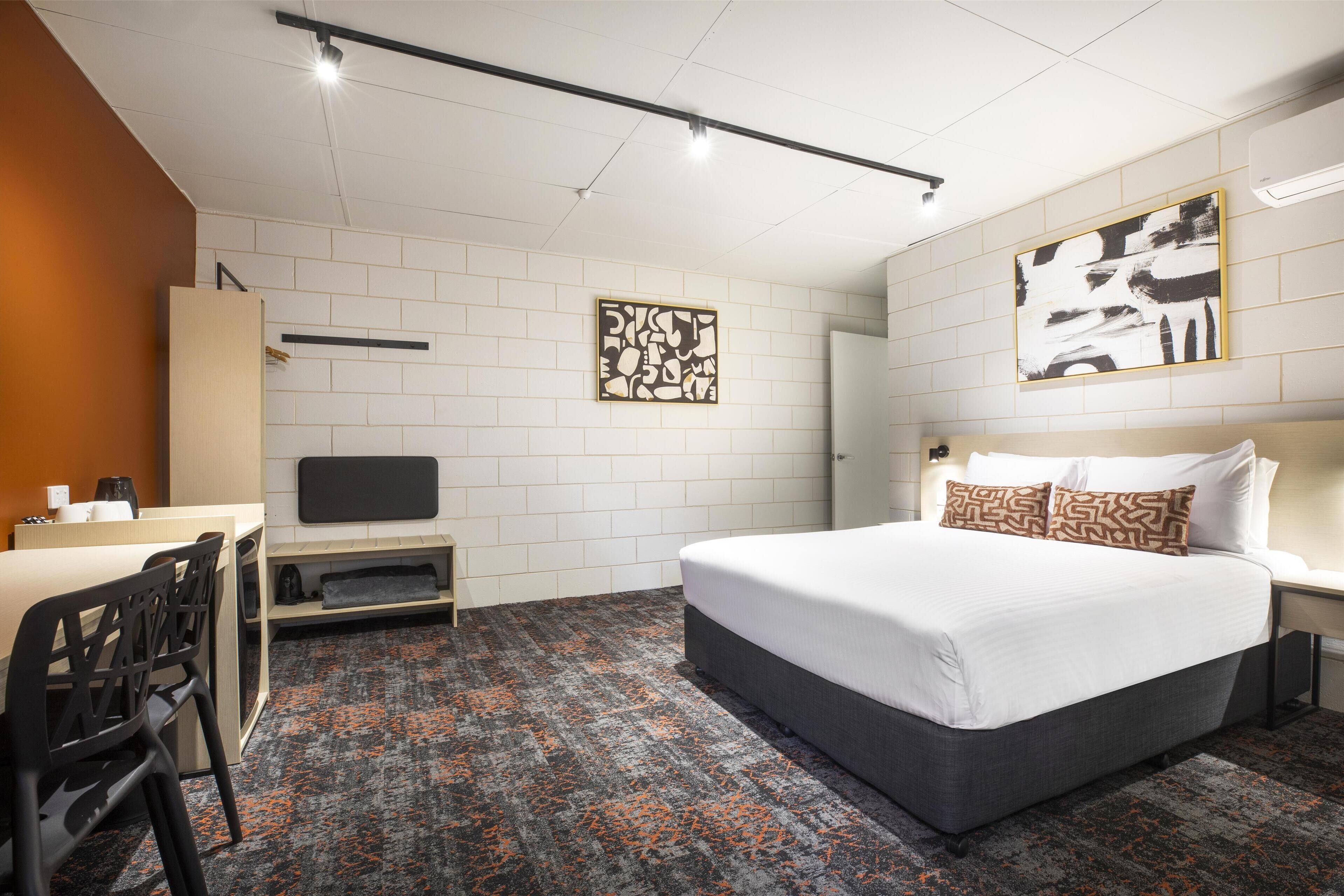 Une chambre d’hôtel avec un lit, un bureau et une chaise. Il y a une télévision sur le bureau et un tableau au mur.