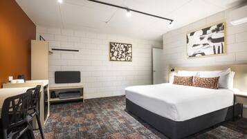 Une chambre d’hôtel avec un lit, un bureau et une chaise. Il y a une télévision sur le bureau et un tableau au mur.
