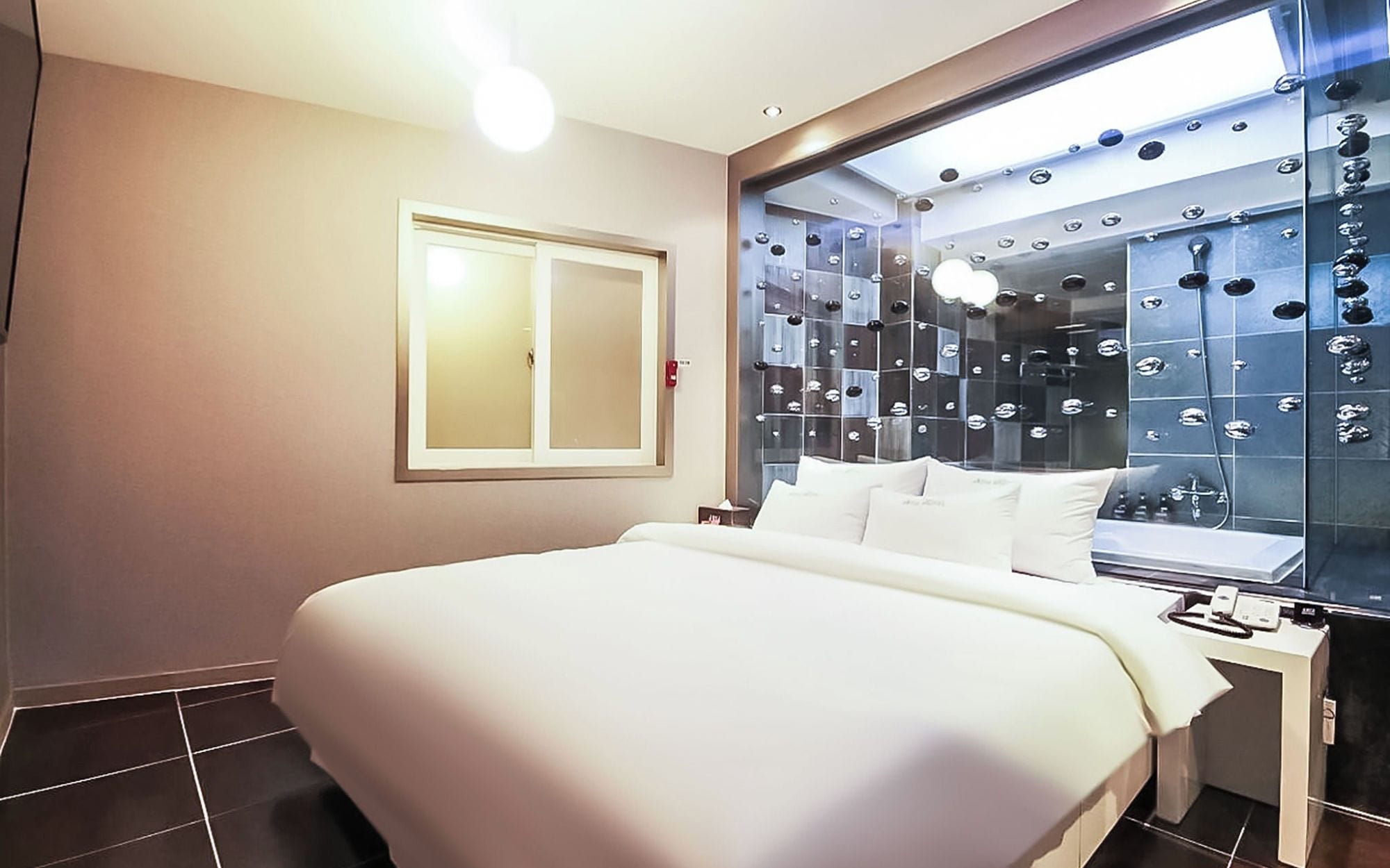 A hotel room with a large bed, a bedside table with a phone, and a wall with a decorative mirror.