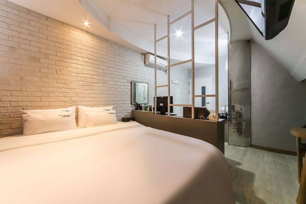 A modern hotel room with a large bed, a brick accent wall, a large mirror, and a TV.