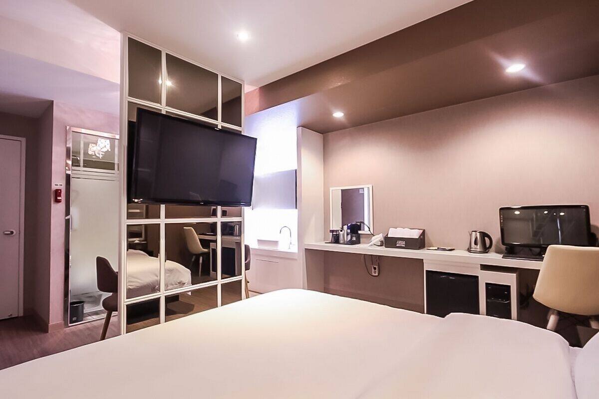 A hotel room with a bed, a TV, a desk with a computer, a chair, and a wardrobe.