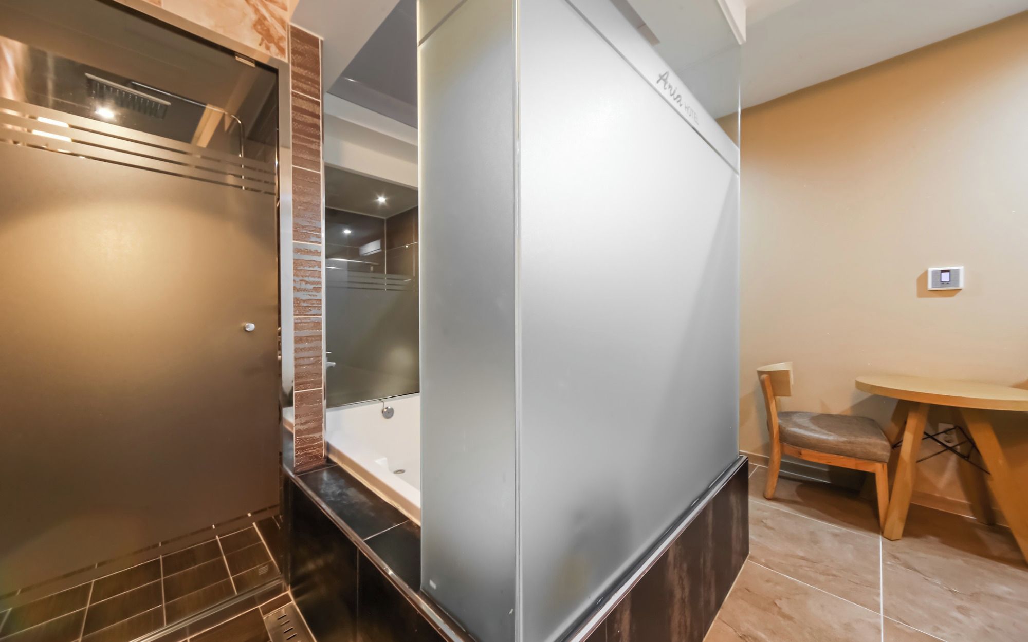 A modern bathroom with a glass shower enclosure, a wooden bench, and a small table.