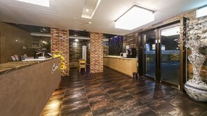 A modern hotel lobby with a reception desk, a brick accent wall, a large decorative vase, and a view through the glass doors. - Hotel Aria Nampo (Busan)