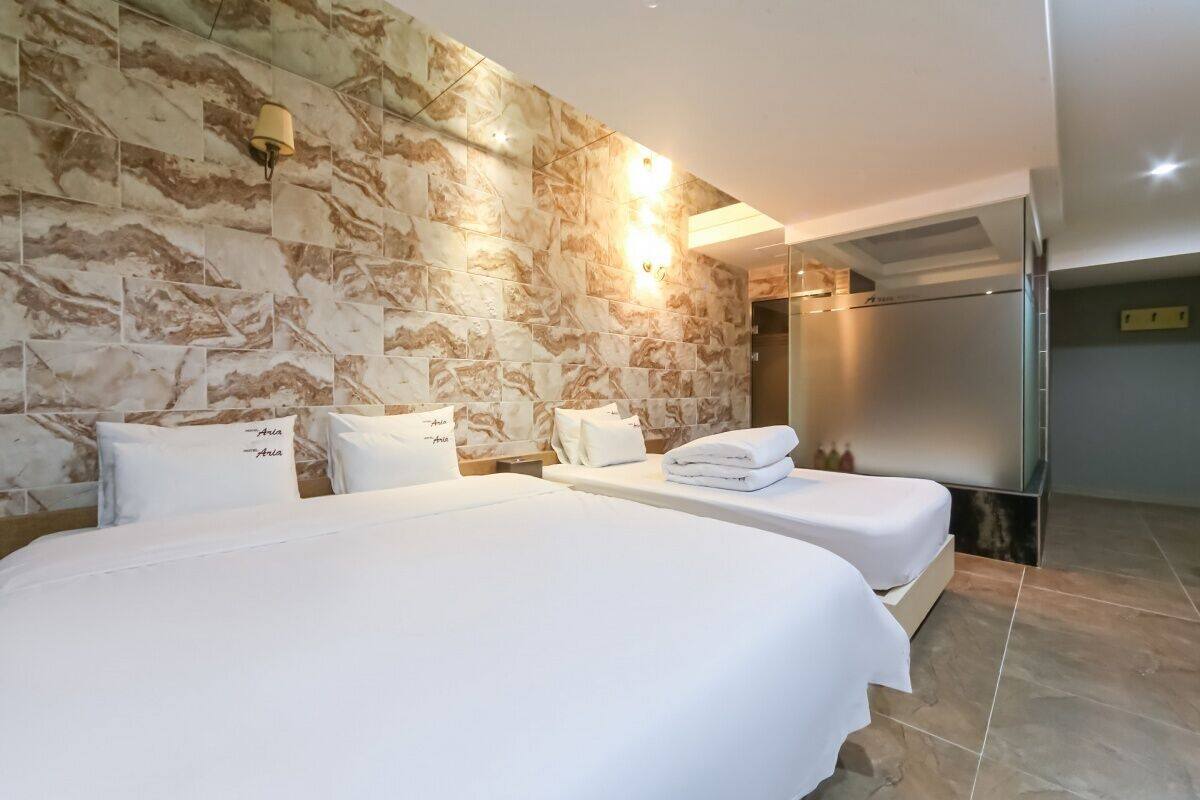 A hotel room with two beds, marble wall, and a modern light fixture.