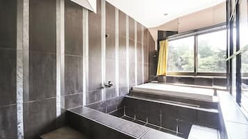 A modern bathroom with a large bathtub, a shower area, and a window providing a view of greenery outside.